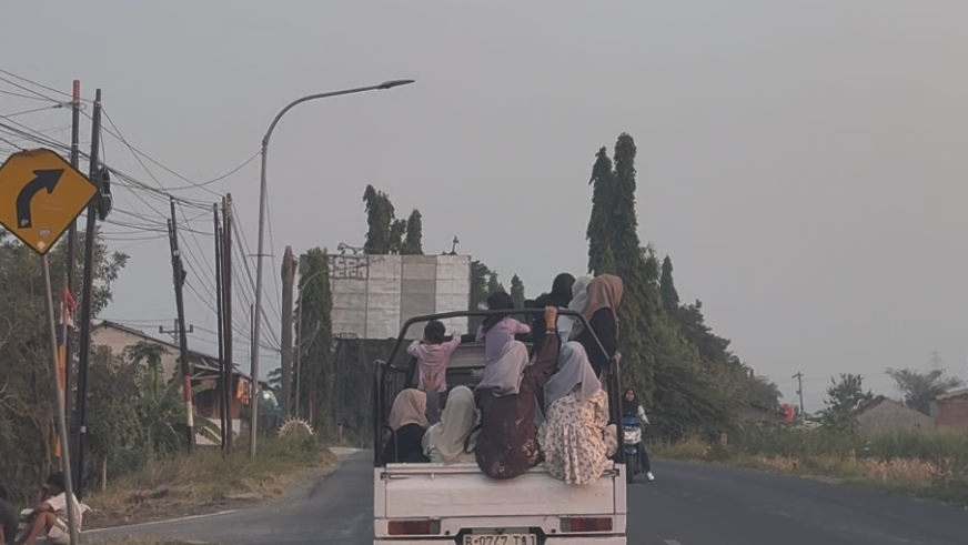 A group of women riding in the open back of a pickup truck on a road near Tegal, Central Java