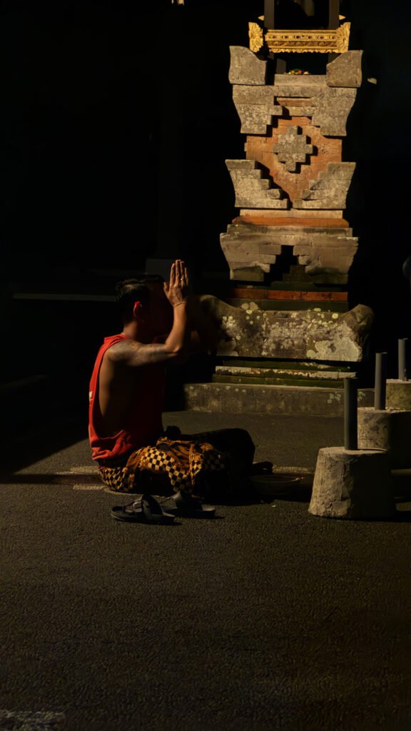 Person praying beside a Balinese shrine in Ubud, Bali, illuminated by warm light.