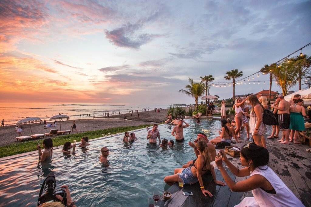 Sunset at a beach club in Canggu, Bali, with travelers gathered around an infinity pool overlooking the ocean.