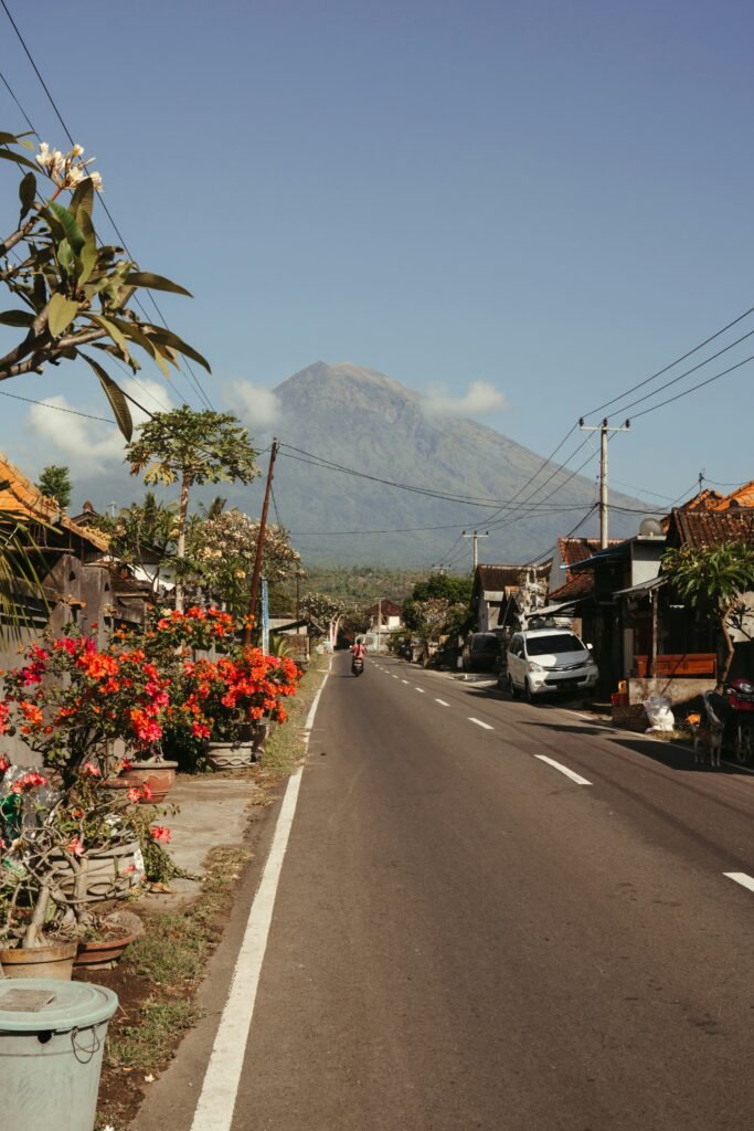 Street in Amed, Bali, with Mount Agung rising behind traditional homes and tropical vegetation.
