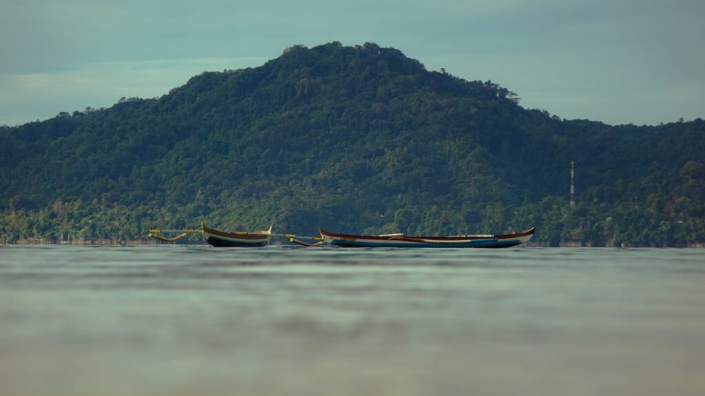 One week in Maluku: two wooden outrigger boats on calm water below a forested hill.