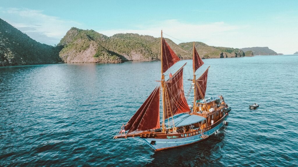 One week in Raja Ampat: a wooden phinisi with red sails on turquoise water beside green islands.